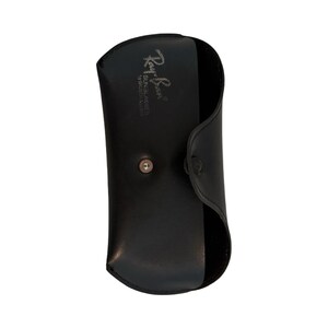 Może przedstawiać: Czarne sk&oacute;rzane etui na okulary przeciwsłoneczne z zapięciem na zatrzask. Etui ma wytłoczone logo Ray-Ban. Zaprojektowane do ochrony okular&oacute;w przeciwsłonecznych.