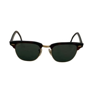 May include: Classic sunglasses with a dark brown and black frame, gold-colored bridge, and dark green lenses. The sunglasses have a retro style and are suitable for both men and women.