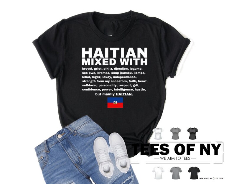 Puede incluir: Camiseta negra con texto blanco que dice "Haitian Mixed With" y enumera varias palabras y frases haitianas. El texto tambi&eacute;n incluye la bandera haitiana. La camiseta est&aacute; sobre un fondo blanco con un par de jeans y zapatillas blancas.