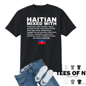 Puede incluir: Camiseta negra con texto blanco que dice "Haitian Mixed With" y enumera varias palabras y frases haitianas. El texto tambi&eacute;n incluye la bandera haitiana. La camiseta se combina con jeans azules y zapatillas blancas.