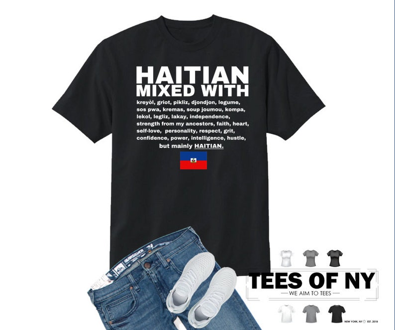 Puede incluir: Camiseta negra con texto blanco que dice "Haitian Mixed With" y enumera varias palabras y frases haitianas. El texto tambi&eacute;n incluye la bandera haitiana. La camiseta se combina con jeans azules y zapatillas blancas.