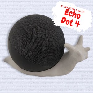 Puede incluir: Un soporte en forma de caracol gris y blanco diseñado para sostener un altavoz inteligente Amazon Echo Dot de 4.ª generación. El soporte está hecho de un material texturizado y tiene una base lisa y redondeada. El texto "COMPATIBLE CON Echo Dot 4" está escrito en rojo sobre un fondo blanco.