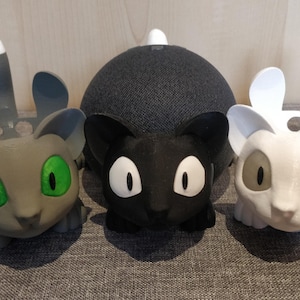 Peut inclure: Trois housses d'enceinte en forme de chat imprimées en 3D en gris, noir et blanc. Les housses ont de grands yeux et un petit nez.