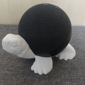 Op de afbeelding: Een zwarte, met stof beklede luidspreker met een witte 3D-geprinte schildpadstandaard.