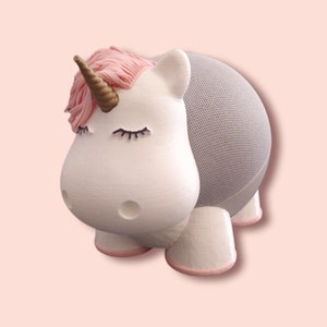 Peut inclure: Un haut-parleur Bluetooth en forme de licorne blanche avec une crinière et une corne roses. Le haut-parleur a une grille en maille grise à l'arrière.