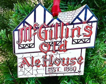 Op de afbeelding: Een witte kerstversiering in de vorm van een gebouw met rode letters die "McGuilins Old Ale House Est 1860" lezen.