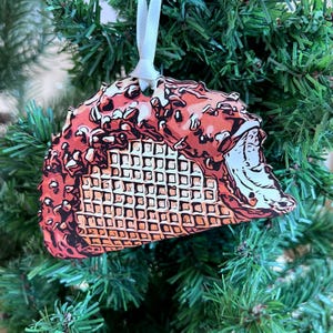 May include: A Christmas ornament shaped like an ice cream cone with a waffle cone and red and white ice cream with chocolate sprinkles.