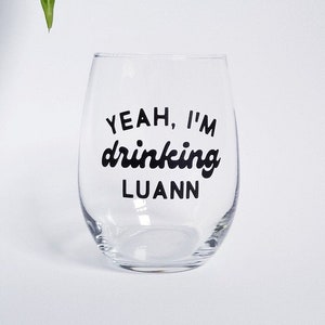 May include: A clear glass wine glass with the text "YEAH, I'M drinking LUANN" printed in black.