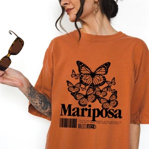 May include: A rust-colored oversized t-shirt with a black butterfly graphic and the word "Mariposa" printed on the front.