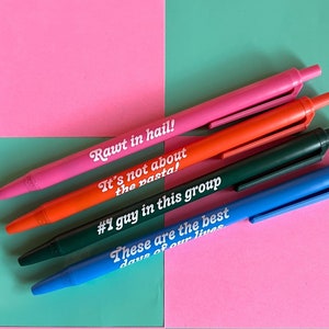 May include: Five colorful pens with different humorous sayings printed on them. The sayings are "Rawt in hail!", "It's not about the pasta!", "#1 guy in this group", and "These are the best days of our lives".