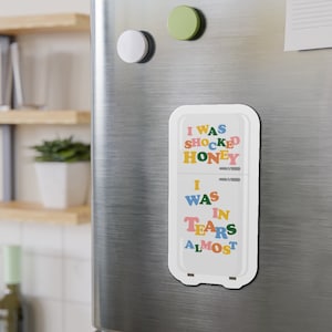 K&ouml;nnte beinhalten: Ein wei&szlig;er K&uuml;hlschrankmagnet mit dem Text "I was shocked honey I was in tears almost" in bunten Buchstaben.