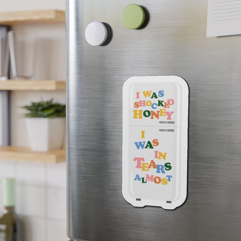 K&ouml;nnte beinhalten: Ein wei&szlig;er K&uuml;hlschrankmagnet mit dem Text "I was shocked honey I was in tears almost" in bunten Buchstaben.
