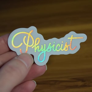 May include: A white sticker with a rainbow iridescent finish that says "Physicist" in a cursive font.