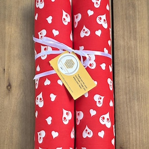 May include: Two cylindrical fabric bolsters in red with a white pattern of hearts and paw prints. The bolsters are tied together with a white ribbon and feature a yellow tag with a honeycomb logo and the text: Thank you for your purchase. I hope you enjoy your item! https://hivecraftycreations.etsy.com