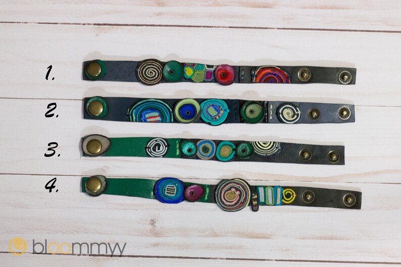 Op de afbeelding: Vier leren armbanden met kleurrijke, gepatroneerde en textuurrijke versieringen. De armbanden zijn genummerd van 1 tot en met 4.