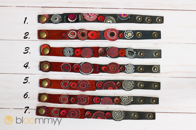 Op de afbeelding: Zeven leren armbanden met rode, witte en zwarte ronde ontwerpen. De armbanden zijn genummerd van 1 tot en met 7.