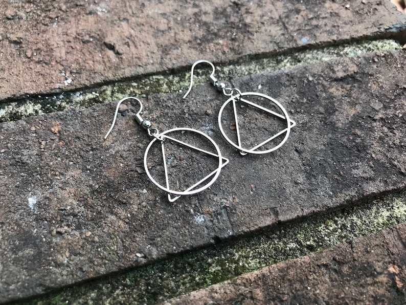 K&ouml;nnte beinhalten: Ein Paar silberne Ohrringe mit einem Kreis- und Dreiecksdesign.