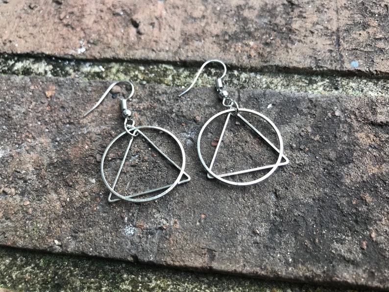 K&ouml;nnte beinhalten: Ein Paar silberne Ohrringe mit einem Kreis- und Dreiecksdesign.