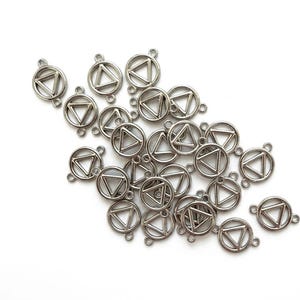 Könnte beinhalten: Eine Sammlung von silberfarbenen Metallanhängern, die jeweils einen kreisförmigen Außenrahmen mit einem mittigen Dreieck aufweisen. Jeder Anhänger verfügt über zwei kleine Ösen an gegenüberliegenden Seiten zur Verbindung mit Schmuck.
