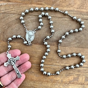Könnte beinhalten: Ein silberfarbener Rosenkranz aus glatten, runden Perlen, die durch eine Kette verbunden sind. Der Rosenkranz enthält eine zentrale ovale Medaille mit der Darstellung des heiligen Michael und ein Kruzifix mit den Buchstaben INRI oben.