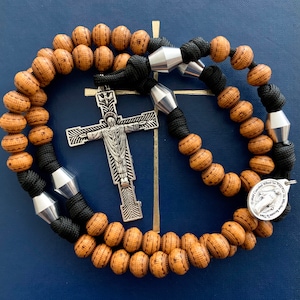 May include: A brown wooden rosary with black cord and silver crucifix and medal. The medal has the words "Other Counsel Without Supreme" and "For the Time Being" on it.