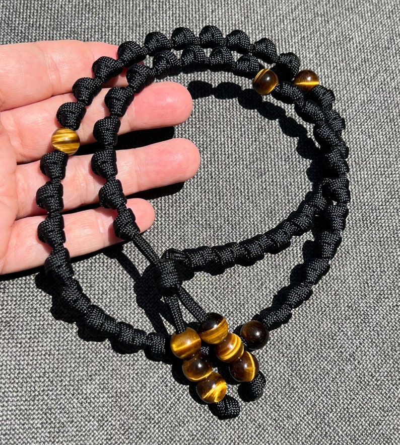 Op de afbeelding: Zwart paracord armband met tijgeroog kralen. Het armband is geknoopt en heeft een kwast aan het einde.
