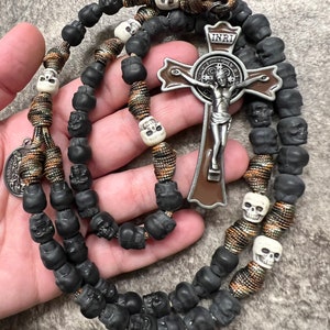 May include: A black and brown rosary with skull beads and a silver St. Francis of Assisi crucifix with the inscription "INRI".