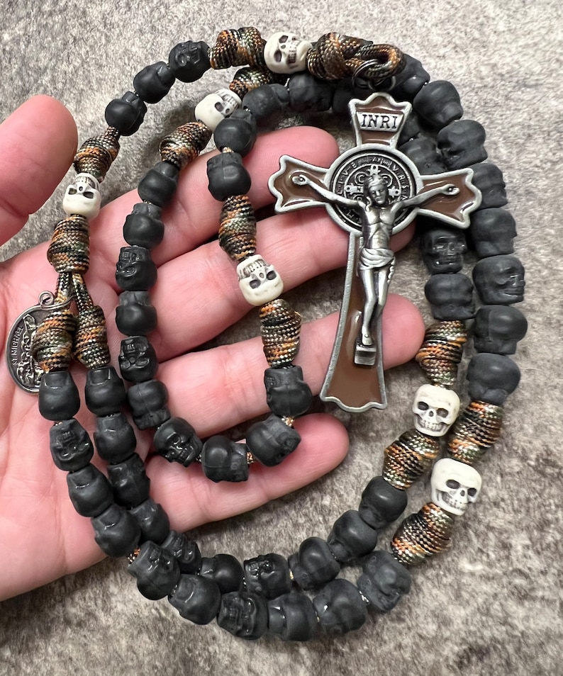 May include: A black and brown rosary with skull beads and a silver St. Francis of Assisi crucifix with the inscription "INRI".