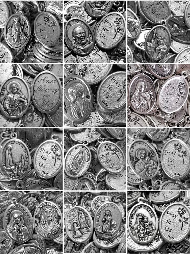 May include: A collection of silver oval-shaped religious medallions with various images and text, including "Pray for Us" and "Have Mercy on Us".