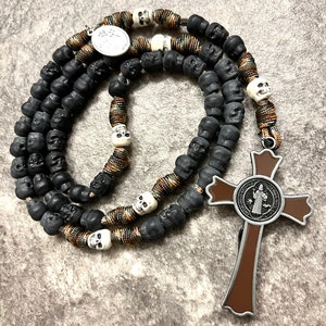May include: A black and brown paracord rosary with skull beads and a brown St. Benedict medal.