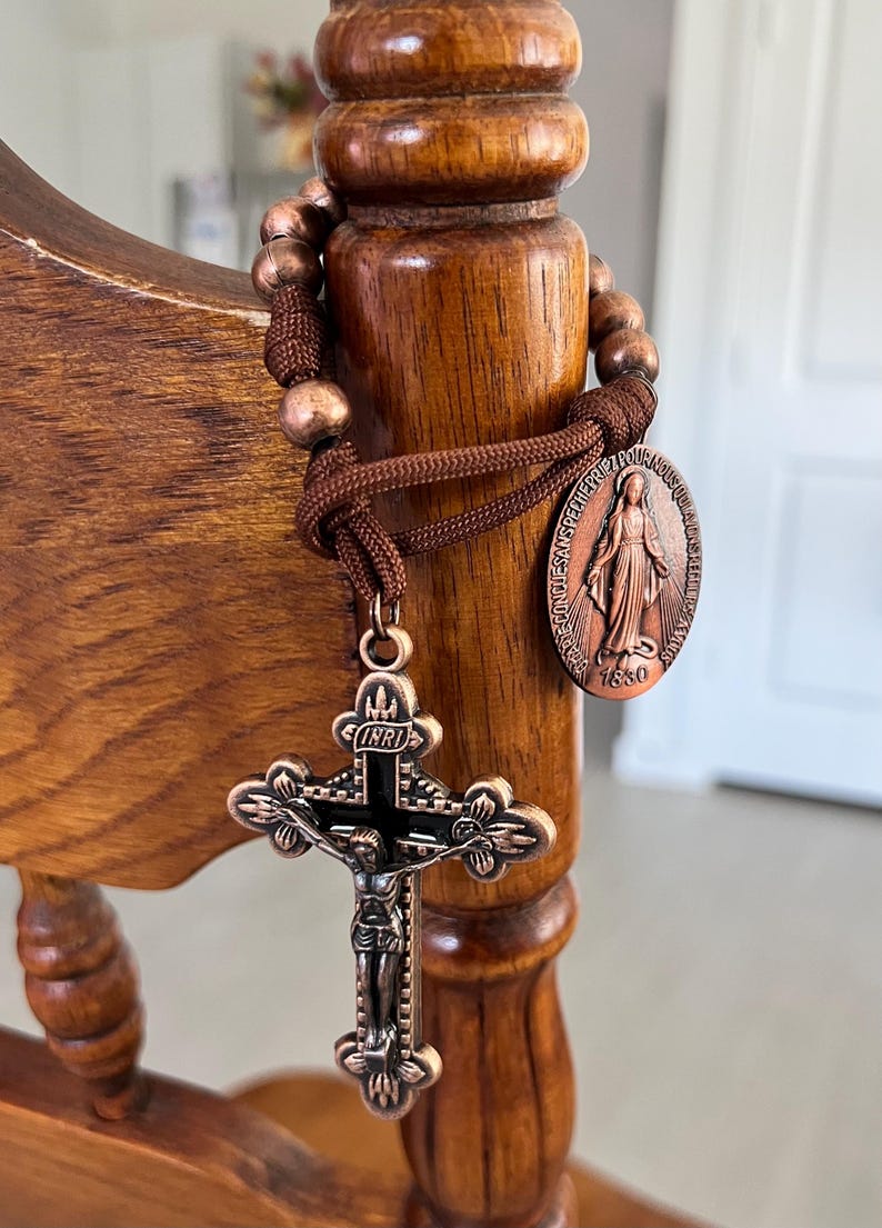 May include: A bronze rosary with a crucifix and a medallion featuring a religious figure. The rosary is wrapped around a wooden post. The crucifix has a detailed depiction of Jesus Christ.