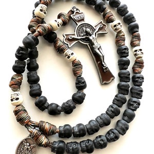 May include: A black and white skull rosary with a brown and silver crucifix featuring the inscription "INRI". The rosary also includes a silver charm with the image of Saint Michael.