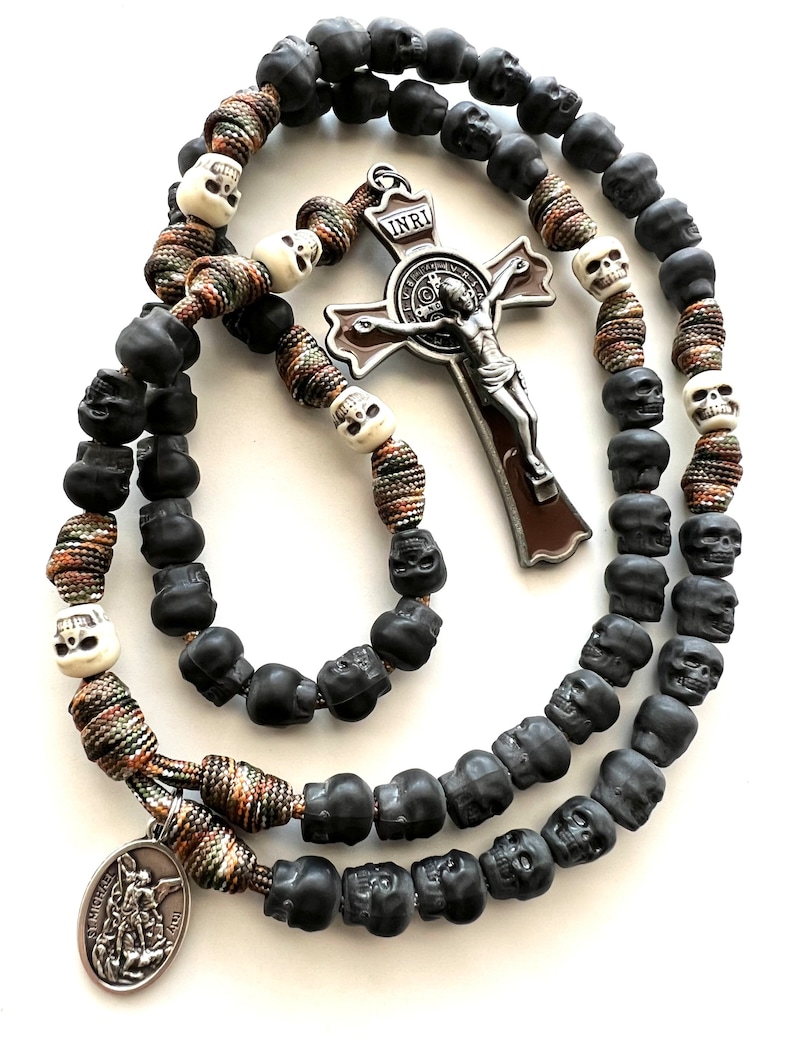 May include: A black and white skull rosary with a brown and silver crucifix featuring the inscription "INRI". The rosary also includes a silver charm with the image of Saint Michael.