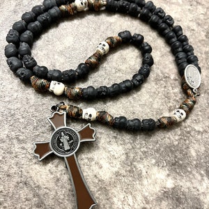 May include: A black and brown rosary with skull beads and a brown cross with a Saint medal.