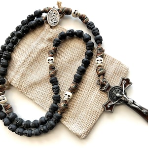 May include: A black and white skull rosary with a brown and silver St. Francis of Assisi crucifix. The rosary is on a beige burlap bag.