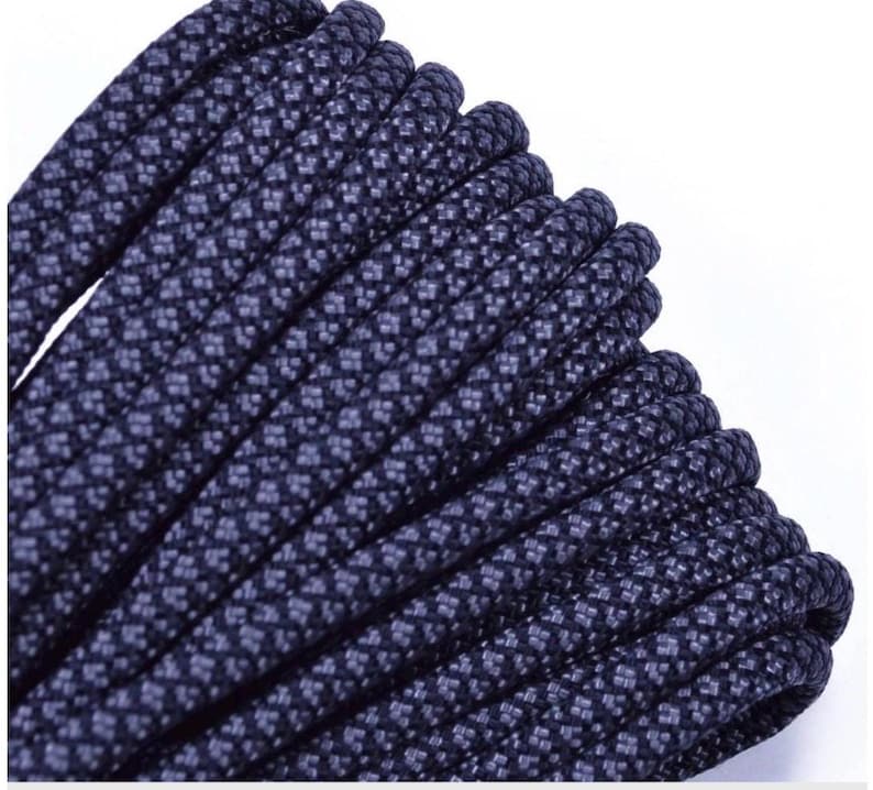 May include: Close-up of a tightly coiled, dark navy blue rope. The rope has a textured surface with a repeating pattern of small, lighter blue squares. The rope is thick and appears durable, suitable for various outdoor and crafting projects.