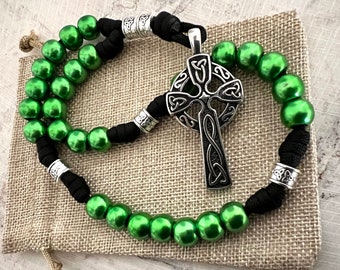 May include: A green beaded rosary with a Celtic cross pendant. The rosary is made with green beads and black cord. The pendant is a silver Celtic cross with intricate knotwork.