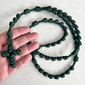 May include: A dark green paracord rosary with a knotted cross. The rosary is made of a durable, braided cord and features a simple, yet elegant design.