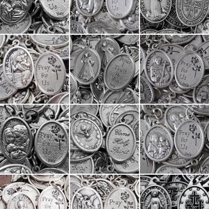 May include: A collection of silver oval-shaped religious medallions with various images and text. The medallions feature images of saints, religious symbols, and text such as "Pray for Us" and "Jesus I Trust in You".