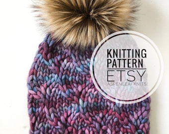 May include: A hand-knitted beanie in shades of purple, blue, and pink, topped with a large, fluffy brown faux fur pom-pom. The hat features a ribbed knit design and a small leather tag. Text on the image reads "KNITTING PATTERN ETSY ASPENLEAFKNITS".