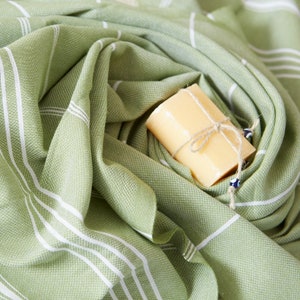 May include: A green and white striped towel with a bar of soap wrapped in twine and a blue evil eye charm.