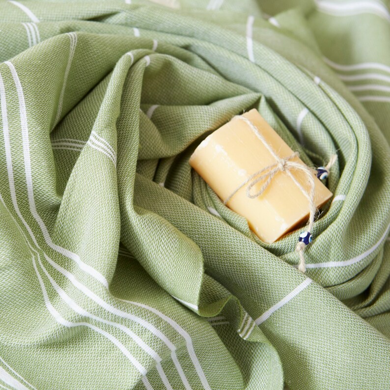 May include: A green and white striped towel with a bar of soap wrapped in twine and a blue evil eye charm.