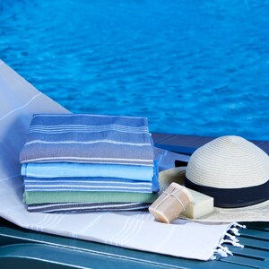 May include: A stack of striped towels in blue, green, and gray colors, a straw hat with a black band, and two bars of soap on a white towel on a green lounge chair by a pool.