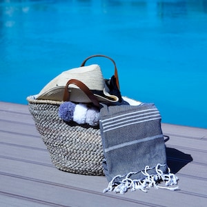 May include: A woven basket with a straw hat, a gray and white pom pom, and a striped gray and white beach towel.