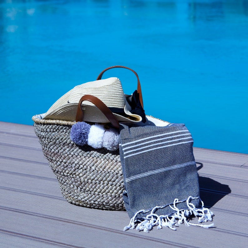May include: A woven basket with a straw hat, a gray and white pom pom, and a striped gray and white beach towel.