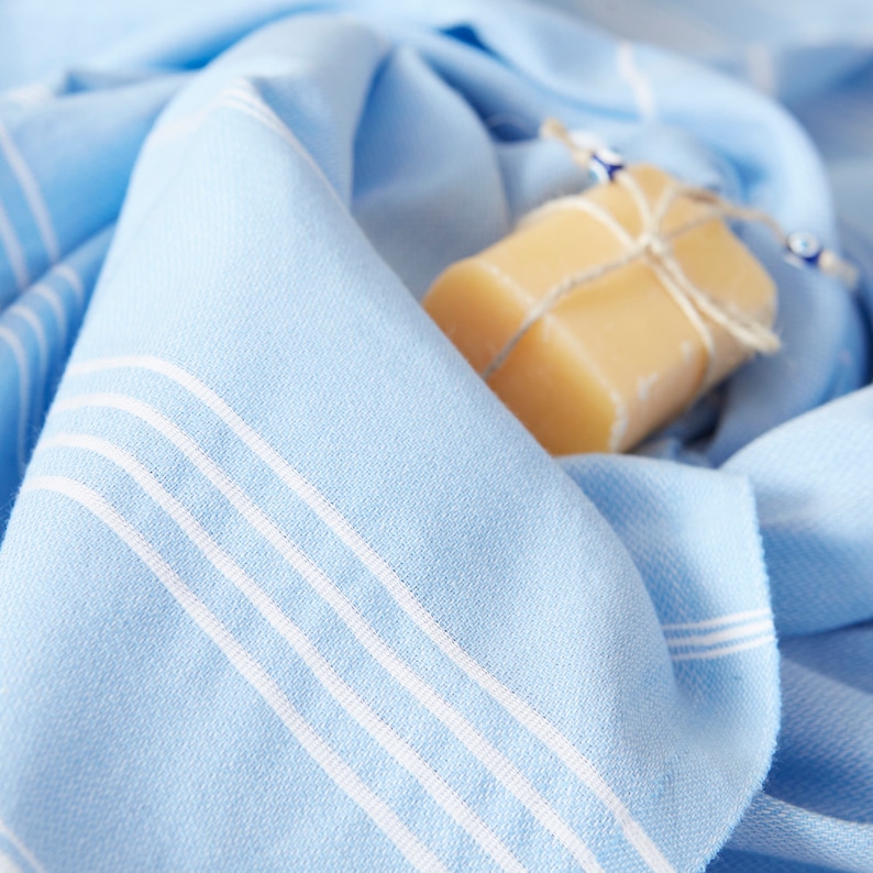 May include: A light blue Turkish towel with white stripes, folded and draped over a bar of soap. The soap is wrapped in twine and has a natural, beige color.