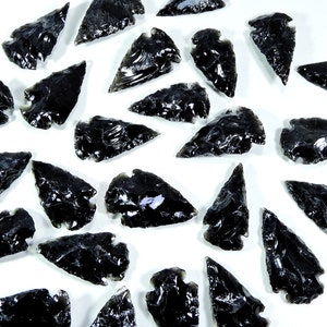 May include: A collection of black obsidian arrowheads, also known as obsidian points, on a white background. These arrowheads are made of volcanic glass and have a sharp, pointed tip.