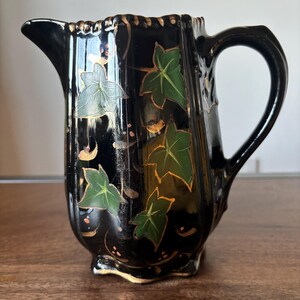 May include: Black ceramic jug with a gold trim and green and white ivy leaf design.