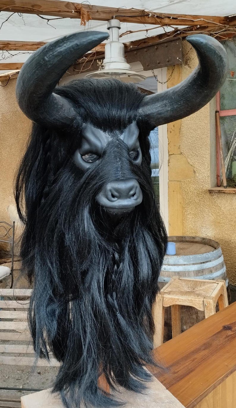 May include: A black bull mask with long, shaggy hair and horns. The mask is made of a hard material and has a realistic appearance.