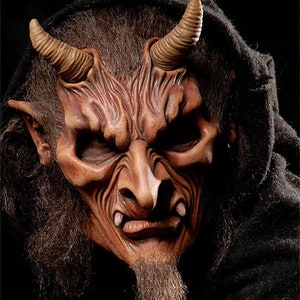 May include: A close-up of a red and brown devil mask with horns, a beard, and a menacing expression.